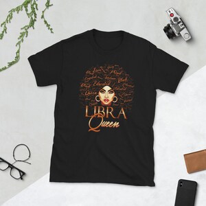 May include: Black t-shirt featuring a brown illustration of a woman with an afro. The afro is made up of words describing a woman's personality. The text "LIBRA QUEEN" is below the illustration.