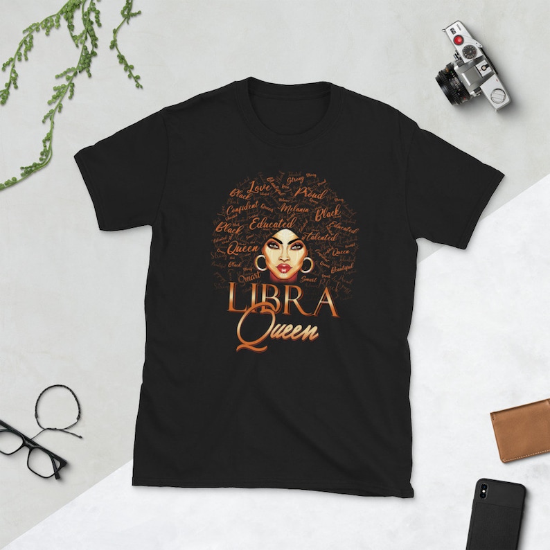 May include: Black t-shirt featuring a brown illustration of a woman with an afro. The afro is made up of words describing a woman's personality. The text "LIBRA QUEEN" is below the illustration.