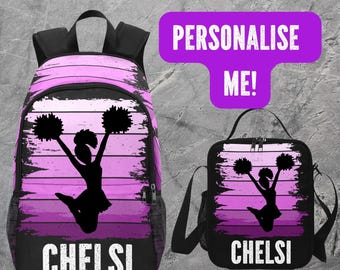 Könnte beinhalten: Ein schwarzes Rucksack- und Lunchpaket-Set mit einer Cheerleader-Silhouette in einem lila-schwarzen Design. Der Rucksack und die Lunchtasche tragen den Namen "CHELSI" in weißen Blockbuchstaben. Der Text "PERSONALIZE ME!" befindet sich in einer lila Blase.