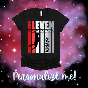 May include: Black t-shirt with a red, white, and gray striped design. The design features a silhouette of a person hanging from a bar with the word "ELEVEN" above and the name "KAYDEN" below.