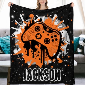 May include: Black and orange personalized throw blanket with a video game controller graphic and the name "JACKSON" in white.