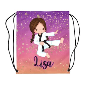 May include: Drawstring bag with a cartoon illustration of a girl in a karate uniform kicking. The background is a gradient of pink and purple with gold glitter accents. The name "Lisa" is written in cursive.
