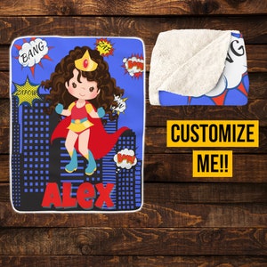 May include: A blue and red personalized superhero blanket with a girl wearing a red cape and a crown. The blanket has a white sherpa backing and the name "Alex" is printed on the front.