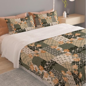 May include: A bedding set featuring a patchwork design with alternating squares of sage green, cream, and black lace patterns, accented with orange floral motifs. The set includes a comforter and two matching rectangular pillow shams.