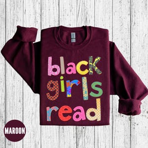 May include: Maroon sweatshirt with the words "black girls read" in colorful patchwork letters.