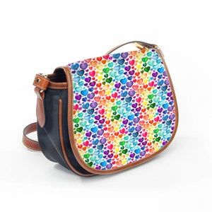 May include: A crossbody bag with a flap closure. The flap features a pattern of colourful hearts on a white background. The bag has a black body with brown leather trim and a brown strap.