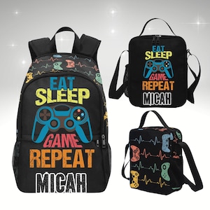 May include: A black backpack, lunch bag, and small bag set with a gaming theme. The backpack and lunch bag feature the text "EAT SLEEP GAME REPEAT" and a controller graphic. The small bag has a controller design and a heartbeat line.
