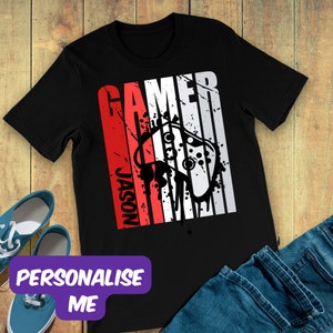 May include: Black t-shirt with a red and white graphic design featuring the word "GAMER" and a game controller. The name "JASON" is printed vertically in red. The phrase "PERSONALISE ME" is in a purple box.