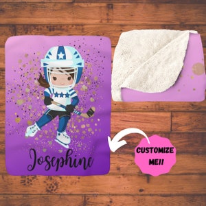 May include: Purple and gold fleece blanket with a cartoon girl wearing a blue hockey uniform and helmet. The girl is holding a hockey stick and is on ice skates. The blanket has the name Josephine on it.