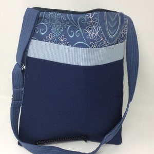 May include: A blue and white patterned crossbody bag with a zipper closure and a long adjustable strap. The bag has a blue fabric lining and a small pocket on the front.