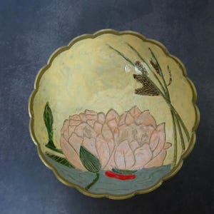 Puede incluir: Un cuenco redondo con borde festoneado, fondo crema y un diseño pintado a mano de una flor de loto rosa con hojas verdes y juncos marrones.