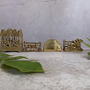 May include: A collection of four brass decorative items including a square openwork pen holder with floral motifs, a rectangular fox figurine by a fence, a semi-circular piece with a lion relief, and a rectangular horse and rider figurine.