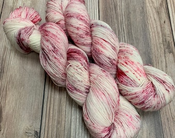 May include: Skeins of white yarn with vibrant red and pink speckles. The yarn is arranged in a twisted pattern, showcasing its texture and color variations. Ideal for knitting or crocheting projects.