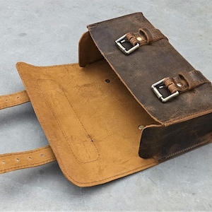 A brown leather tool bag is shown open with its flap down and buckle straps extended on a gray background.