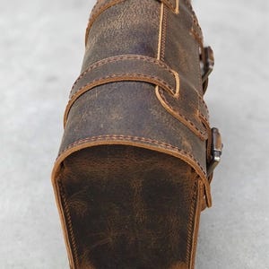 A close-up view of the side panel and curved closure of a brown leather motorcycle tool bag.