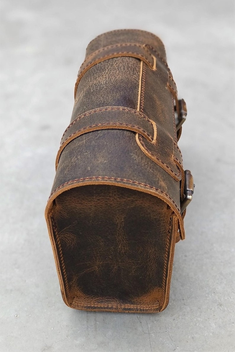 A close-up view of the side panel and curved closure of a brown leather motorcycle tool bag.