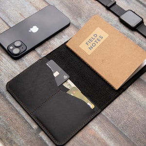 May include: A black leather wallet with a notebook, credit cards, and cash inside. The notebook has the words "Field Notes" on the cover.