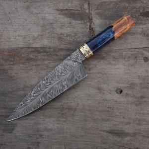 Puede incluir: Un cuchillo de chef de acero Damasco con mango de madera azul. La hoja tiene un patrón ondulado y el mango tiene un acento dorado.