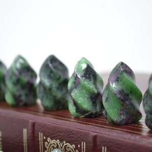 May include: A row of six green, black, and purple swirl-shaped stones on a red book. The stones are polished and have a smooth, shiny surface.