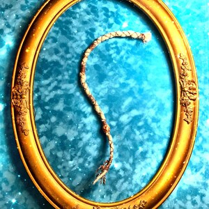 Peut inclure: Un cordon tressé blanc et brun avec une perle en bois suspendu dans un cadre ovale doré sur un fond bleu avec des étoiles blanches.