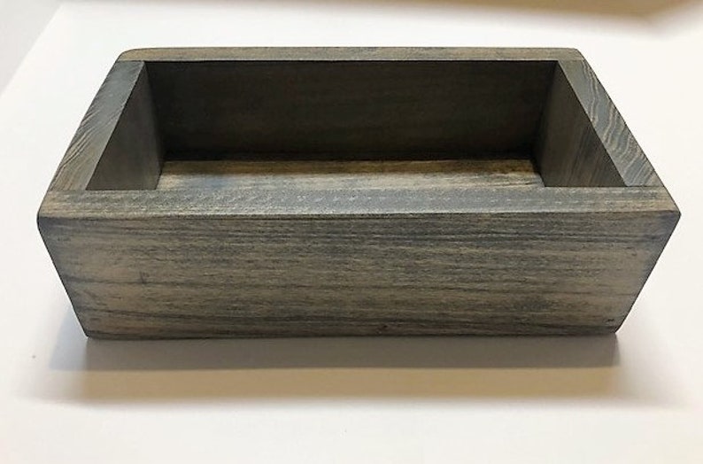 May include: A rectangular wooden box with a gray wash finish. The box has a simple design and is perfect for storing small items.