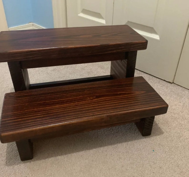 May include: A dark brown wooden step stool with two steps. The top step is wider than the bottom step.