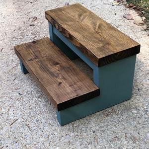May include: A two-step wooden stool with a teal blue base and a dark brown stained top. The stool is made of solid wood and has a rustic look.
