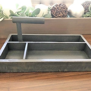 May include: A gray wooden tray with three compartments and a black metal handle. The tray is on a wooden surface.