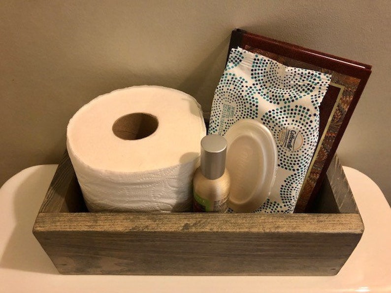 May include: A rustic wooden box with a roll of toilet paper, a package of facial tissues, a small bottle of hand sanitizer, and a disposable plate. The box is gray and has a distressed finish.