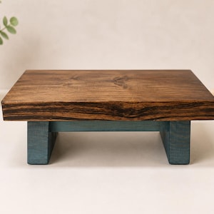 May include: A rectangular wooden riser featuring a dark brown stained top surface with visible wood grain and two sturdy legs painted in a muted blue finish. The stand is constructed with a flat platform supported by two vertical block-style legs.