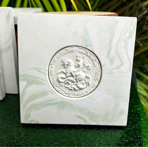 May include: Square, white and green marbled decorative block with a circular, raised relief of a figure on a horse. The relief is surrounded by a Greek key border. The block is part of a set, with other blocks visible in the background.