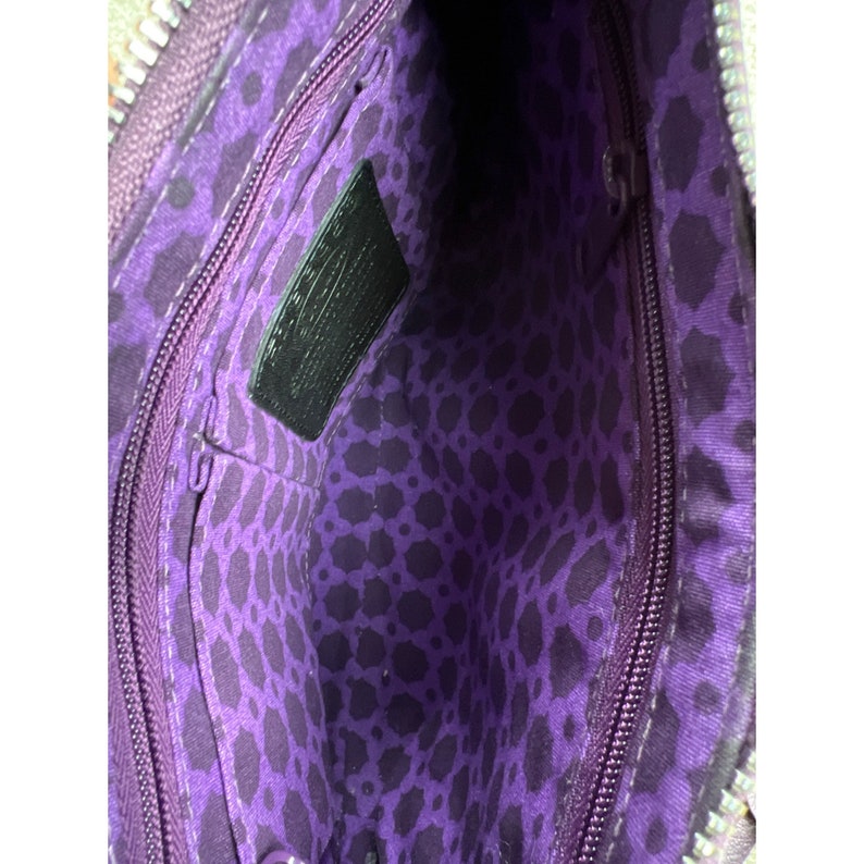 May include: Purple and black leopard print fabric lining the inside of a handbag. The handbag has a zipper closure and a small interior pocket. The interior pocket has a black leather tag with the word "Coach" embossed on it.