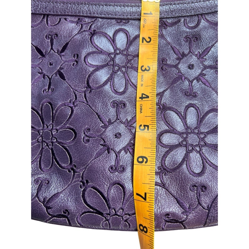 May include: Purple leather clutch with a floral embossed design. The clutch measures 7 inches in length.