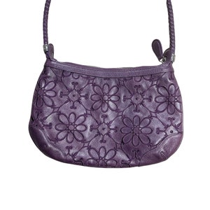 May include: A purple leather handbag with a floral embossed design. The bag has a top handle and a shoulder strap.