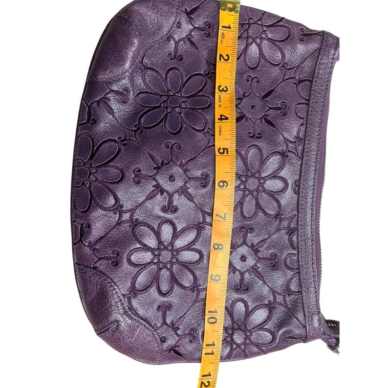 May include: A purple leather clutch bag with a floral design. The bag is approximately 11 inches long.