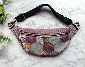May include: A pink corduroy fanny pack with a black adjustable strap and a gold zipper. The front of the pack features a geometric pattern of purple, green, and gold hexagons.