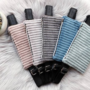 Puede incluir: Cinco riñoneras de pana en diferentes colores: rosa, gris, gris claro, azul y azul claro. Las riñoneras tienen correas y cremalleras negras.