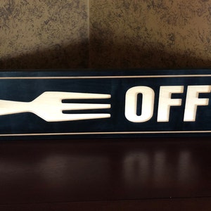 May include: A black wooden sign with a white cutout of a fork and the word "OFF" in white letters.