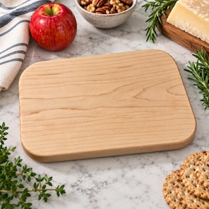 May include: A rectangular wooden cutting board with rounded corners and a smooth, light-toned grain pattern. The board features a flat surface and is positioned centrally, showcasing the natural wood texture and light brown color of the material.