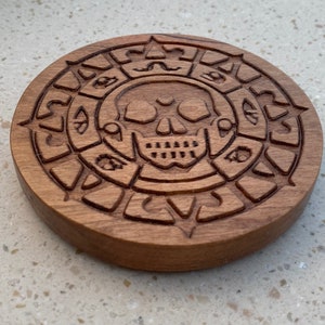 May include: A wooden coaster with a carved skull and a circle of symbols around it.