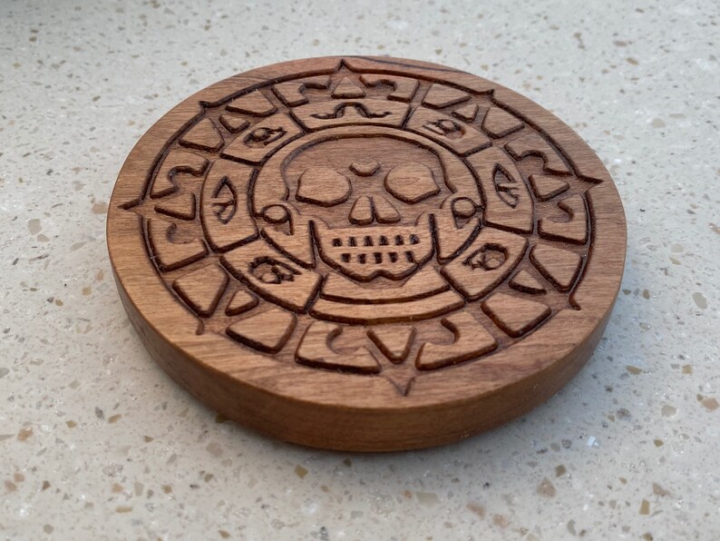 May include: A wooden coaster with a carved skull and a circle of symbols around it.