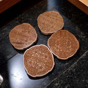May include: Four wooden coasters with intricate Celtic knot designs. The coasters are circular and have a dark brown color.
