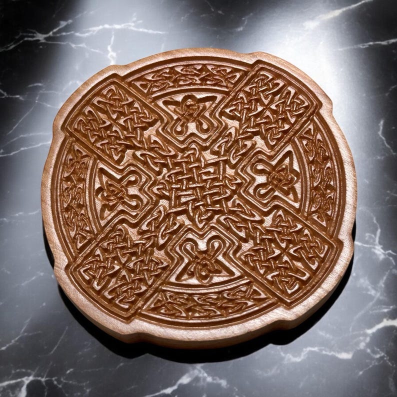 May include: A wooden coaster with a Celtic knot design carved into the surface. The coaster is round and has a brown wood finish.