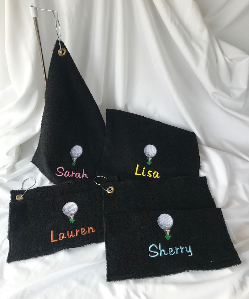 May include: Four black golf towels with embroidered golf balls and names: Sarah, Lisa, Lauren, and Sherry. The names are embroidered in different colors.