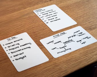 May include: Three white cards with handwritten notes on a wooden surface. One card lists a "To Do" list, another a "Mind Map" for a website, and the third a schedule for Monday, August 26, 2024. The cards are arranged on a light brown wooden table.