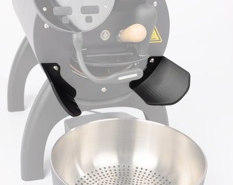 Könnte beinhalten: Schwarzer Kaffeeröster mit einem Auffangbehälter aus Edelstahl. Der Röster hat zwei schwarze Seitenpaneele, die helfen, die Kaffeebohnen in den Auffangbehälter zu leiten.