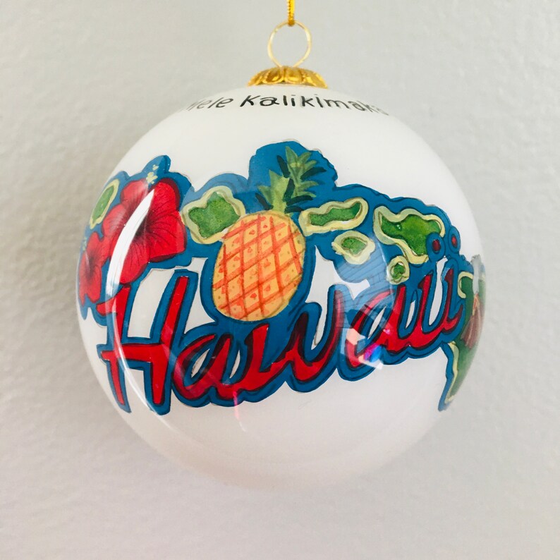 May include: White glass Christmas ornament with a red, yellow, and green pineapple, red hibiscus flowers, and the word "Hawaii" in blue and red lettering. The ornament also features an outline of the Hawaiian islands in green.