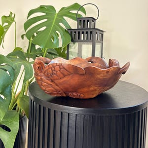 May include: A wooden bowl carved in the shape of a turtle. The bowl is brown and has a natural wood finish. It is sitting on a black table.