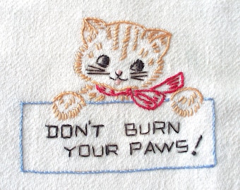 May include: Embroidered kitchen towel with a cute cartoon cat wearing a red bow and holding a sign that says "Don't Burn Your Paws!"