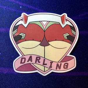 May include: A pink heart-shaped sticker with a cartoon character inside. The character has red and green markings and white horns. The sticker has a pink banner with the word "DARLING" written in white.